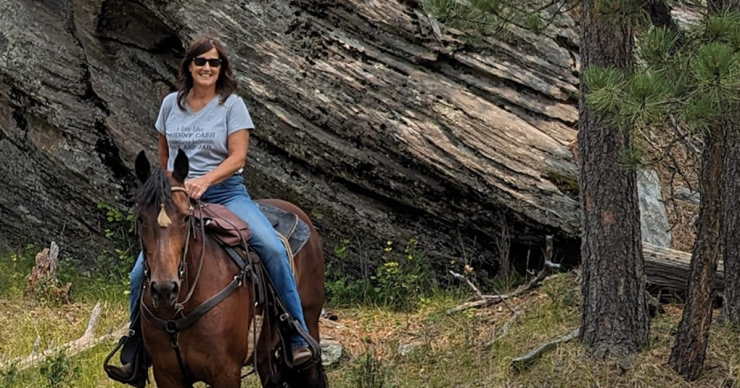 Carla Kaup riding a horse in front of a rock formation.
